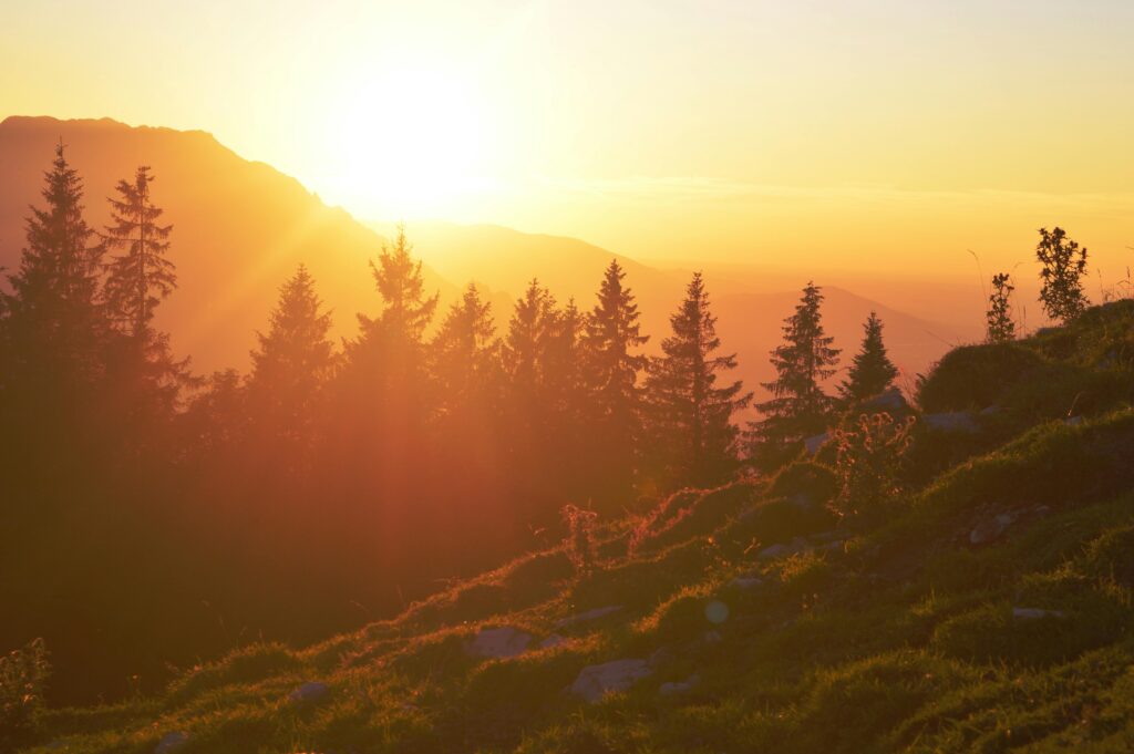 Vibrant sunset over mountain terrain with silhouette of trees and warm orange hues.